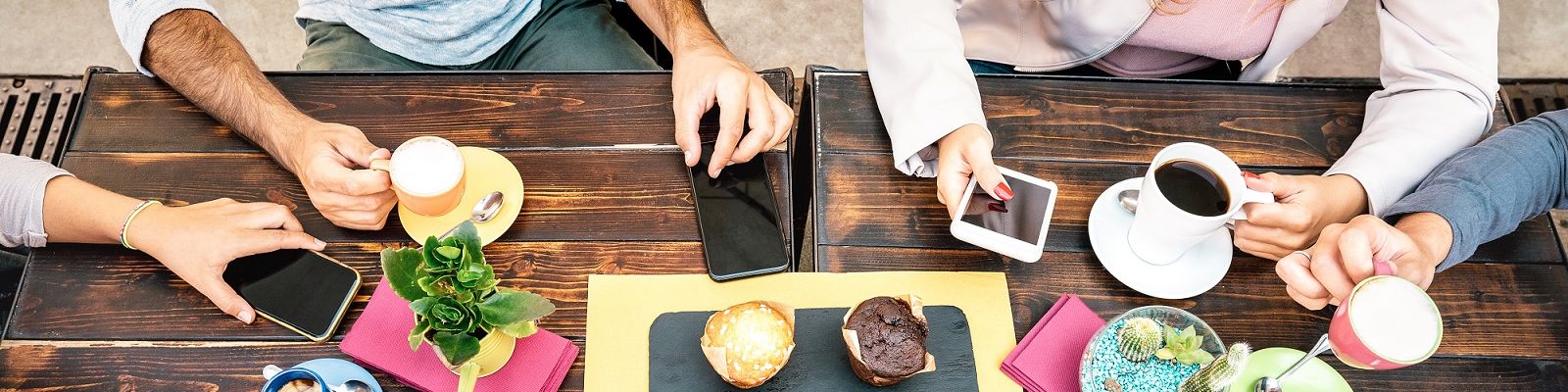 Verschiedene Hände mit Kaffeetassen und Smartphones von oben an einem Holztisch